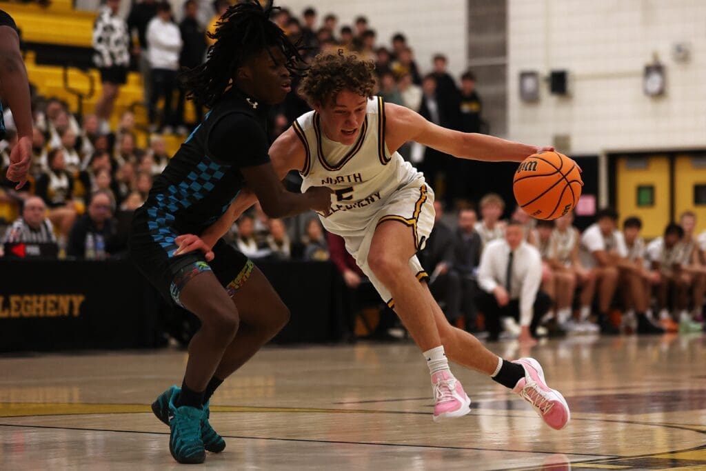 Basketball player dribbles during a high school game, preparing to pass an opponent on the court.