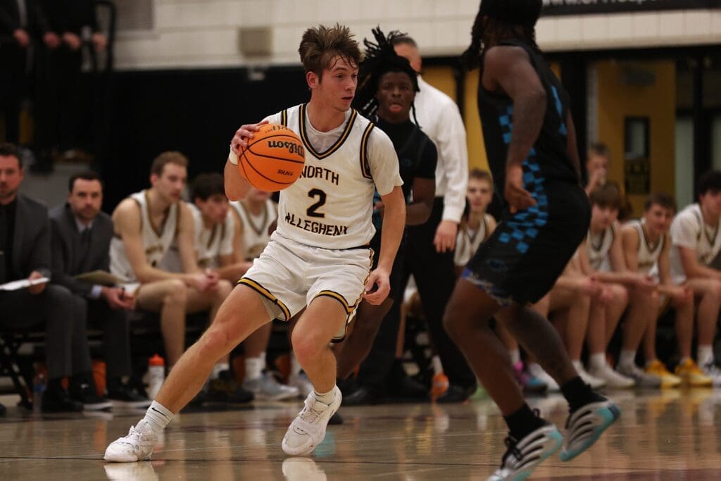 High school basketball player dribbles past defender in an intense game.