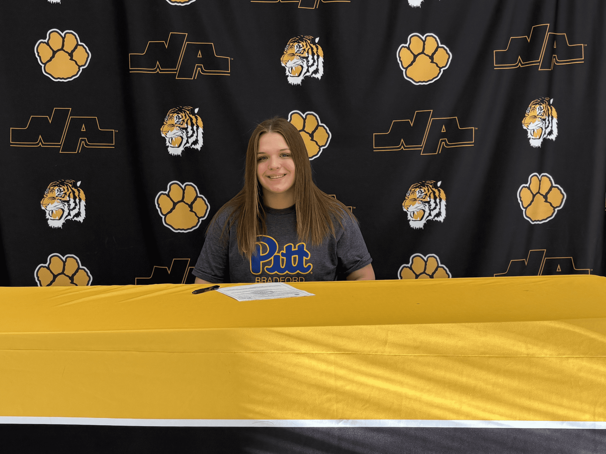 Student athlete celebrating commitment to Pitt Bradford at signing event with North Allegheny banner in the background.