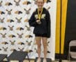 Smiling athlete on podium with medal, wearing North Allegheny rowing gear.