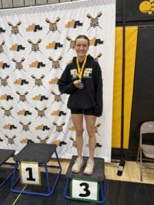 Smiling athlete on podium with medal, wearing North Allegheny rowing gear.