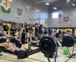 Indoor rowing competition in a gym, with athletes and spectators. USA and tiger decor visible in the background.