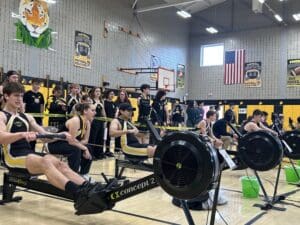 Indoor rowing competition in a gym, with athletes and spectators. USA and tiger decor visible in the background.
