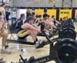 Students compete on rowing machines in a gym during a school event, showcasing teamwork and athleticism.