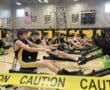 Indoor rowing competition in a gym with athletes in matching uniforms exercising intensely on rowing machines.