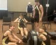 Teen rowers in a competition, gathering around an indoor rowing machine in sports gear, focused and determined.
