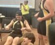Rowing team in action during an indoor competition, focused on an ergometer with cheering teammates nearby.