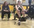 Indoor rowing competition at Marshall Middle School gym, focused athlete on ergometer, coach supervising.