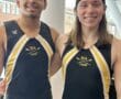 Two rowers in team uniforms standing indoors, smiling, with NA Crew logo visible.