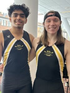 Two rowers in team uniforms standing indoors, smiling, with NA Crew logo visible.