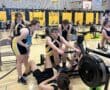 Indoor rowing team practice in gym with athletes focused on technique and teamwork.