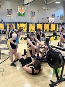 Indoor rowing team practice in gym with athletes focused on technique and teamwork.