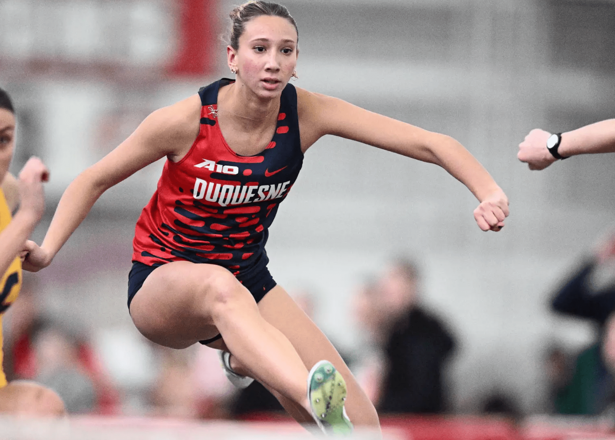 Athlete in Duquesne attire competing in a hurdle race, showcasing focus and determination indoors.
