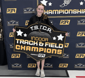 Young athlete celebrates winning TSTCA Indoor Track & Field Championships holding a large champion sign.