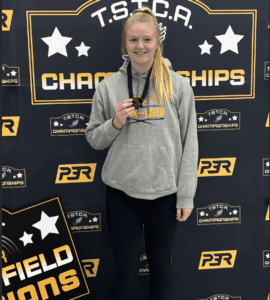Athlete holds medal at TSTCA Track and Field Championships, smiling in front of event banner.