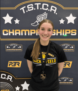 Track athlete smiling with medal, standing in front of TSTCA Championships banner.
