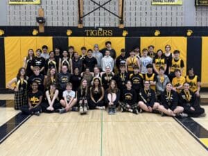 Middle school rowing team group photo in gym, students in matching black and yellow uniforms with medals.