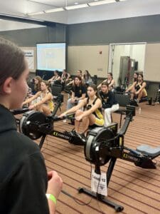 Women competing in an indoor rowing championship, focused and ready on rowing machines.
