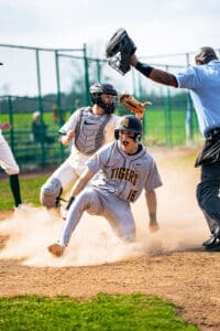 Baseball player sliding into home plate, celebrating while umpire calls the play during a thrilling game moment.