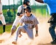 Baseball player sliding into home plate, celebrating the score as the umpire makes a call, surrounded by teammates.