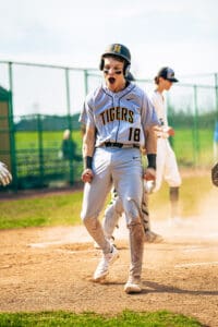 Youth baseball player celebrating at home plate, wearing a Tigers uniform, full of excitement and energy.