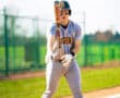 Softball player in a gray uniform preparing to swing a bat on a sunny field, showcasing athletic focus and determination.