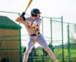 Young baseball player in a gray uniform prepares to hit, showcasing concentration and athletic stance at the batter's box.