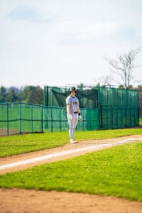 A young baseball player stands on the field, ready for the game, wearing team colors and a helmet.
