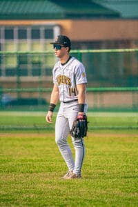 Baseball player in gray Tigers uniform stands on field, ready for action, with glove in hand and sunglasses on.
