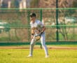 A young baseball player in uniform prepares to field on a sunny day at the ballpark. Green grass and a chain-link fence backdrop.