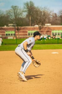 Baseball player in grey uniform crouching ready for play on the field during a sunny day.