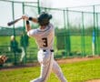 Young baseball player swings a bat during a game, showcasing athletic posture on the field in bright sunlight.