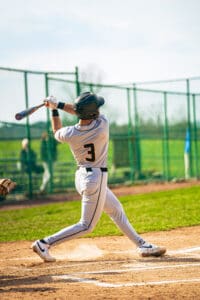 Young baseball player swings a bat during a game, showcasing athletic posture on the field in bright sunlight.