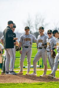 Alt text: Baseball team huddled on the pitcher's mound, discussing strategy during a sunny game day.