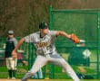 A baseball pitcher in gray Tigers uniform winds up to throw a pitch on a sunny day at the baseball field.