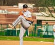 High school baseball pitcher in grey uniform prepares to throw on the mound during a sunny game day.