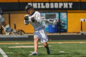 Lacrosse player in action, executing a pass on the field during a sunny day, showcasing athletic skill and teamwork.