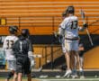 Lacrosse players celebrating a goal during a game on a bright, sunny day with team colors prominently displayed.