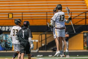 Lacrosse players celebrating a goal during a game on a bright, sunny day with team colors prominently displayed.