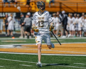 Lacrosse player in action on field, wearing a Tigers jersey and gearing up to play during a sunny game day.