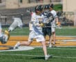 Lacrosse player in white uniform sprinting on the field, preparing to pass the ball during a game.