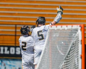 Two lacrosse players celebrate a goal, showcasing teamwork and excitement during a game in bright uniforms.