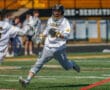 High school lacrosse player in action, sprinting on the field, ready to make a play during a sunny spring practice.