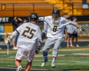 Two lacrosse players celebrate a goal on the field, showcasing teamwork and excitement in a vibrant sports setting.