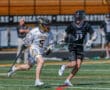 Two young lacrosse players compete fiercely on a bright, sunny field during a high-energy game.