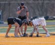 Two lacrosse players face off on a field with a referee overseeing the game, ready for the match to begin.