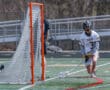 High school lacrosse player in action, wearing a Tigers jersey, attempting to score against the goalie.
