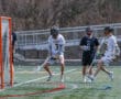 Lacrosse players in action during a game, focused on scoring while defending the goal on a sunny day.