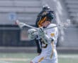 Lacrosse player in action, wearing a helmet and jersey, poised to make a play on the field.