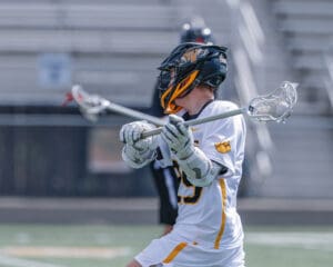 Lacrosse player in action, wearing a helmet and jersey, poised to make a play on the field.